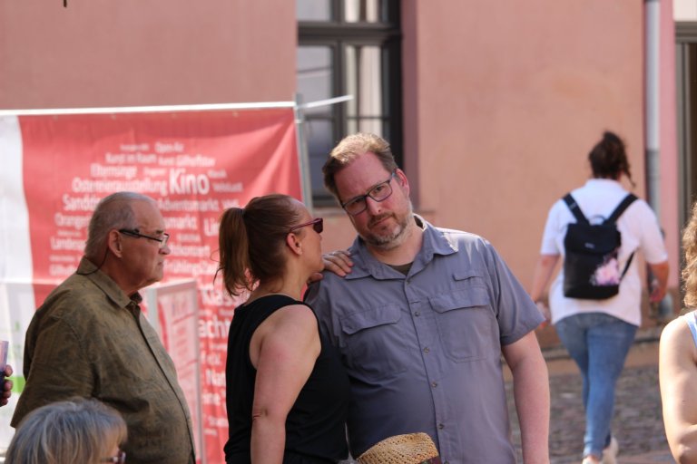 Besucher beim Lindenfest Ludwigslust unterhalten sich vor rotem Informationsbanner der Musicalschule Ahrensburg.