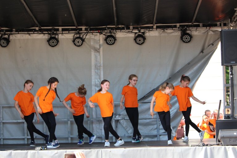Kinder der Musicalschule Ahrensburg führen Tanzperformance in orangenen Shirts beim Lindenfest Ludwigslust auf.
