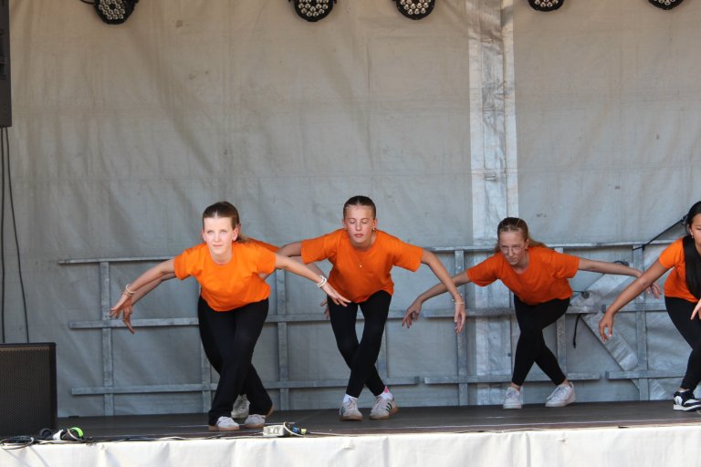 Vier Kinder in orangenen Shirts tanzen synchron auf einer Bühne beim Lindenfest Ludwigslust der Musicalschule Ahrensburg.