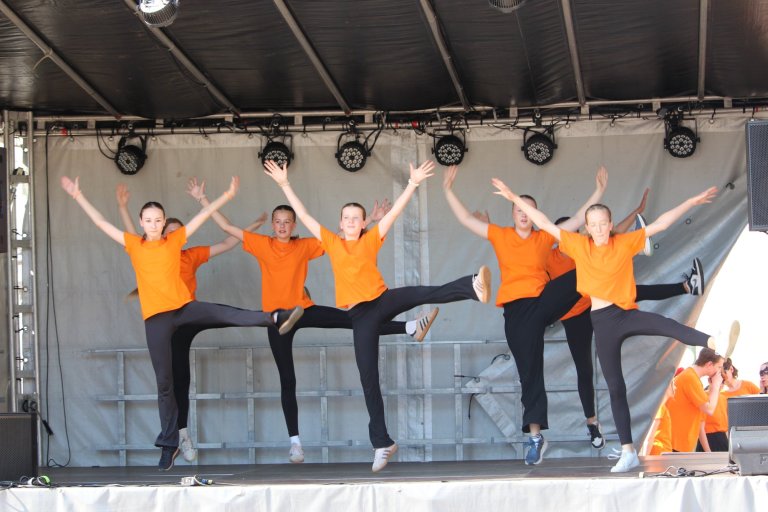 Fünf Schüler der Musicalschule Ahrensburg in orangefarbenen Shirts präsentieren synchron Sprünge auf der Lindenfest-Bühne.