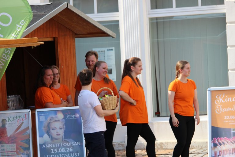 Musicalschüler in orangenen T-Shirts präsentieren Programm beim Lindenfest Ludwigslust vor historischem Gebäude.