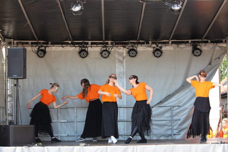 Fünf junge Tänzerinnen in orangen Shirts und schwarzen Röcken tanzen synchron auf einer Außenbühne beim Lindenfest Ludwigslust.