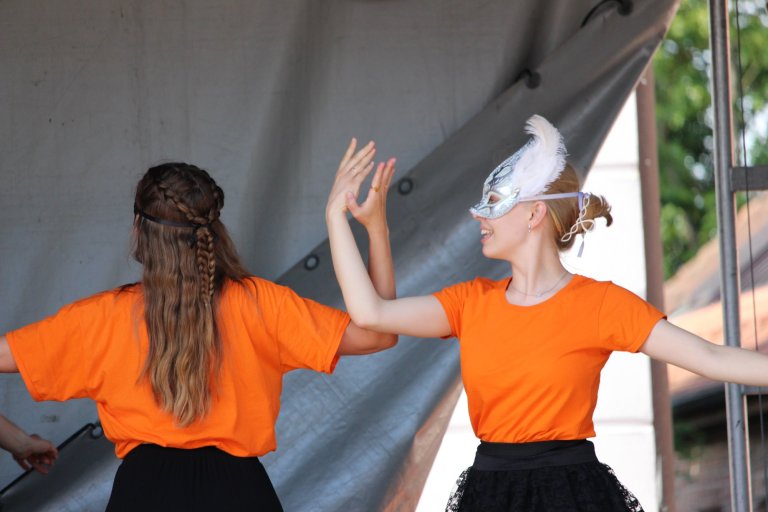 Zwei Schülerinnen in orangenen Shirts führen Tanzperformance mit weißen Masken beim Lindenfest Ludwigslust auf.