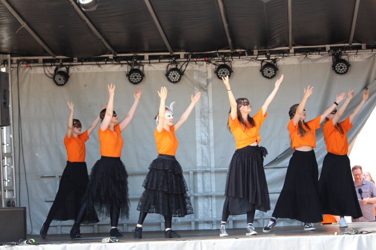 Musicalschule Ahrensburg Tanzgruppe performt auf Bühne beim Lindenfest Ludwigslust in orangefarbenen Tops und schwarzen Röcken.