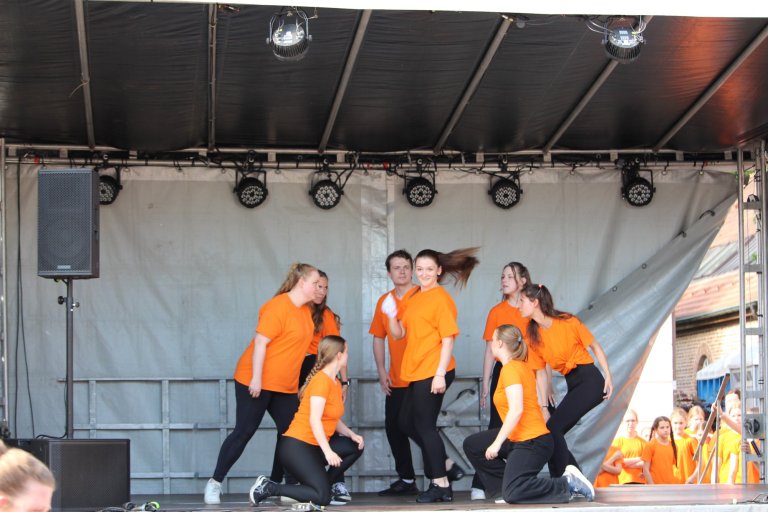 Musicalschüler in orange Shirts performen auf Bühne beim Lindenfest Ludwigslust mit Tänzern und Publikum.
