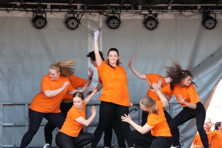 Tanzgruppe in orangefarbenen Shirts führt synchrone Choreografie auf Bühne des Lindenfests Ludwigslust auf.
