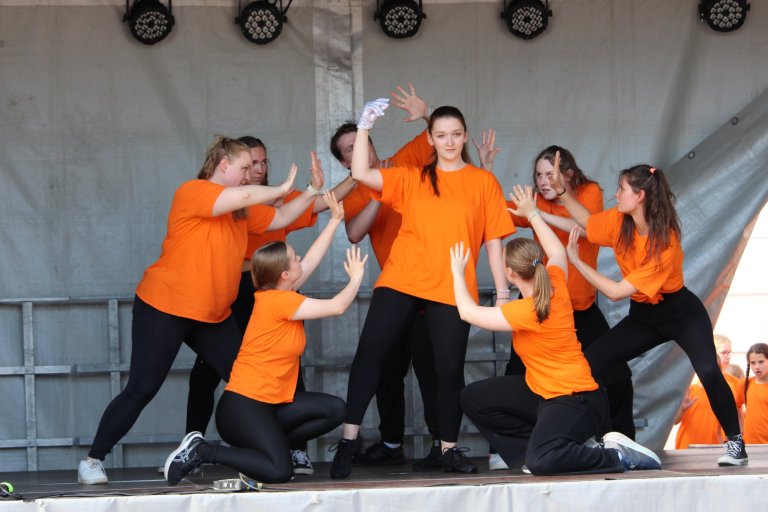Gruppe junger Tänzer in orangen Shirts beim Lindenfest Ludwigslust auf der Bühne, Musicalschule Ahrensburg Performance.