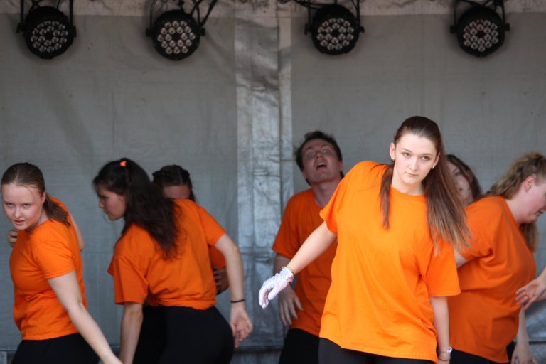 Gruppe junger Performer in orangenen Shirts auf Bühne beim Lindenfest Ludwigslust der Musicalschule Ahrensburg.