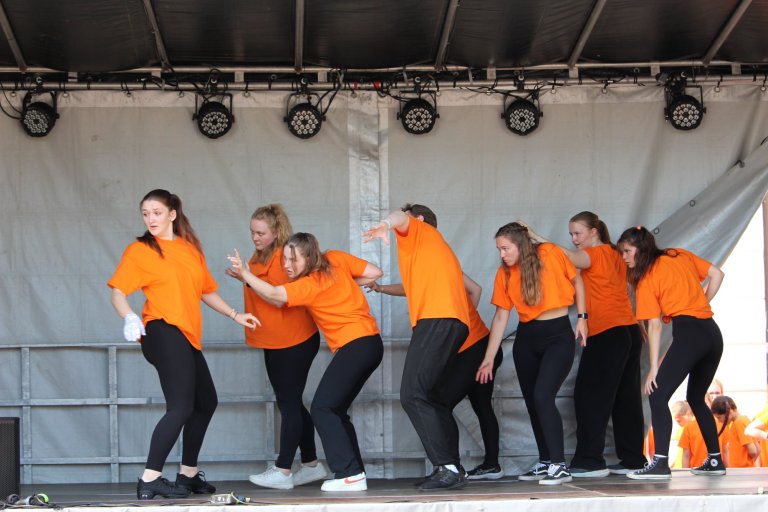 Musicalschulgruppe in orangenen Shirts tanzt synchron auf Bühne beim Lindenfest Ludwigslust auf.